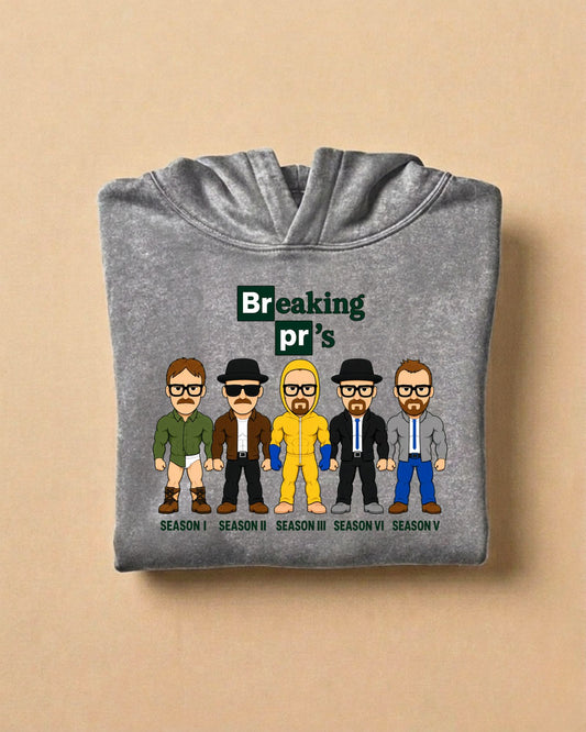 Asphalt grey Breaking pr's oversized washed gym hoodie, folded, front view: tile-style lettering above five cartoon characters in different outfits with season captions
